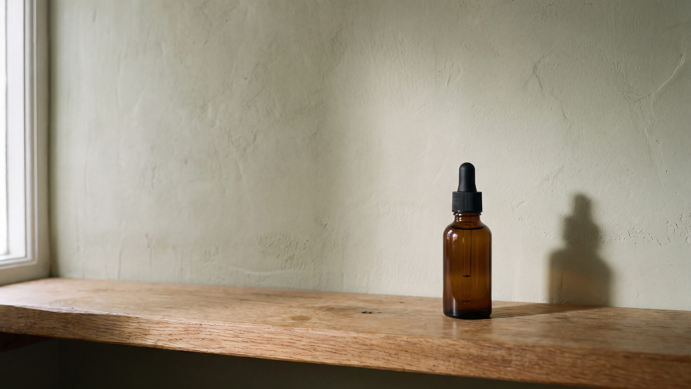 A single amber dropper bottle on an oak shelf against a plastered wall