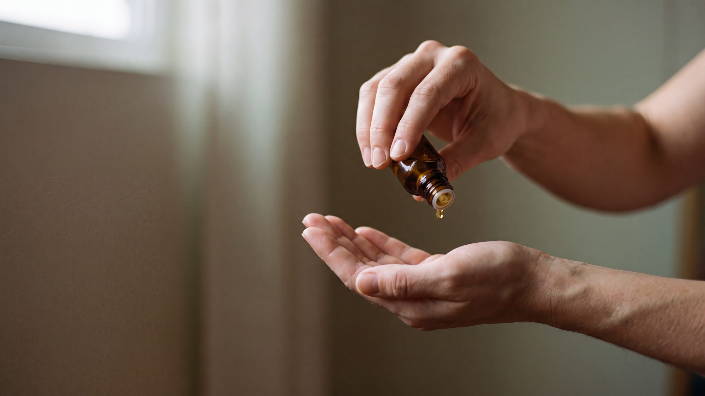 Two hands, one tilting an amber bottle to release oil into the other palm