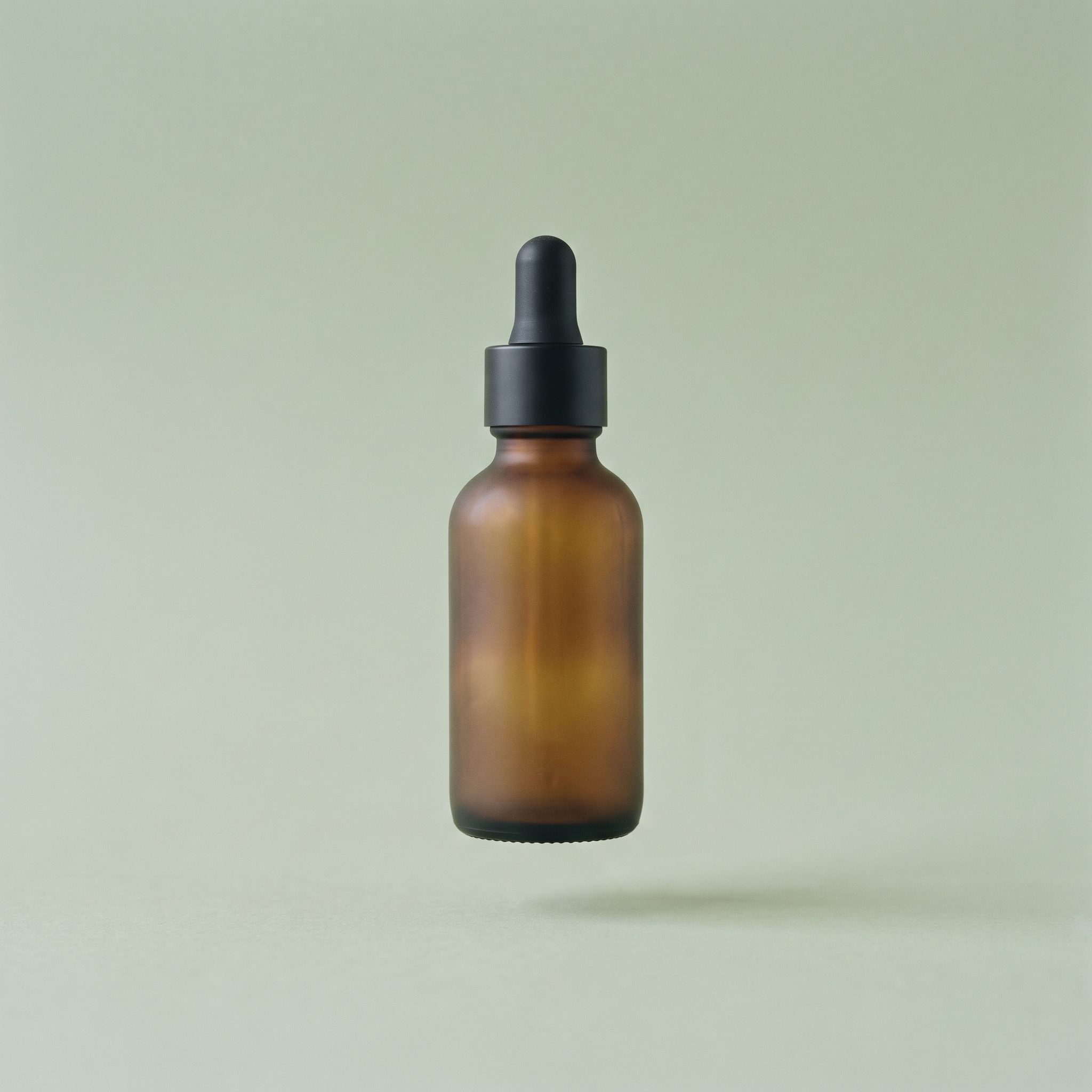 A single amber dropper bottle against a flat pale sage background