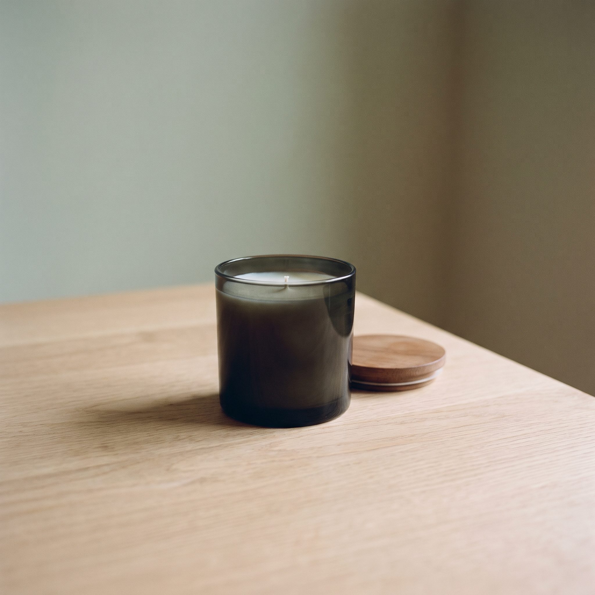 An unlit dark glass candle with its wooden lid resting beside it